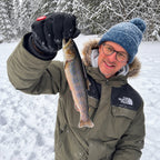 Angler in winter clothing holding a fish above the snow.